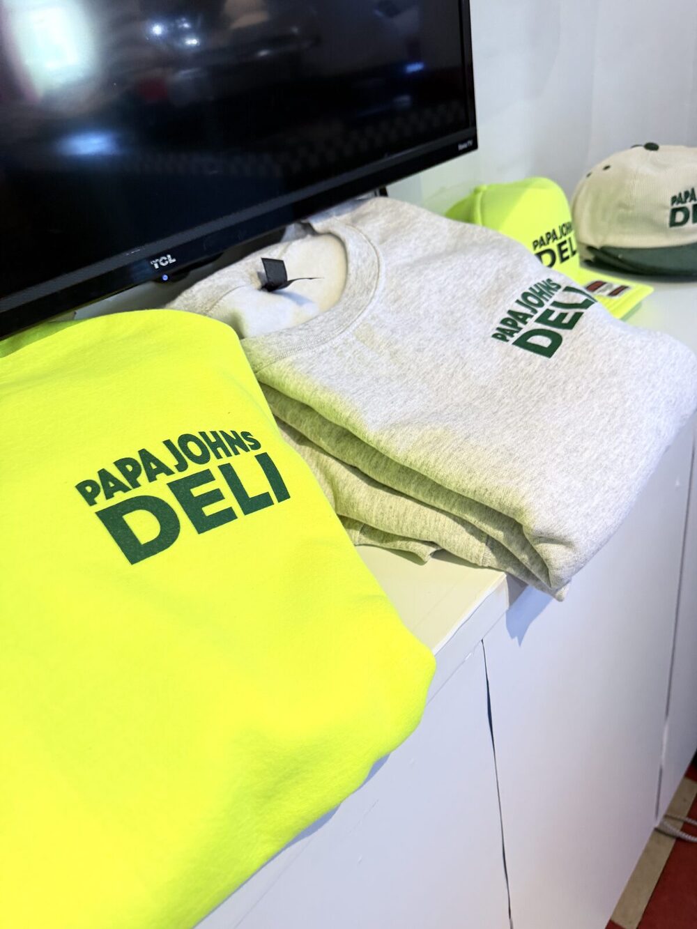 Folded custom-printed sweatshirts in neon yellow and heather grey beside a matching printed corduroy cap