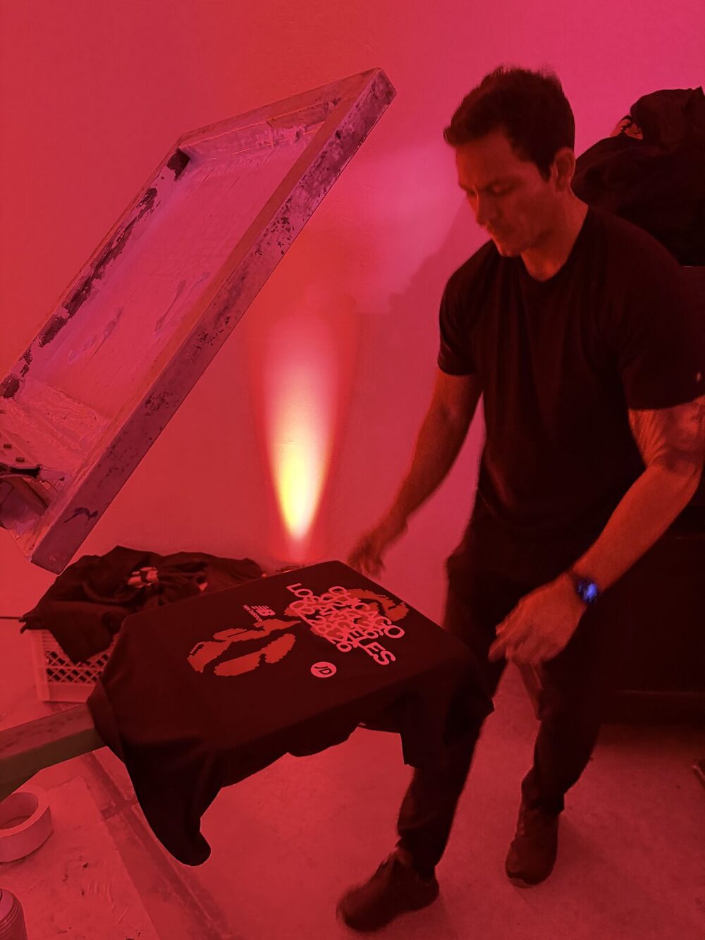 A freshly printed shirt being lifted off the press platen with the inked screen raised above it